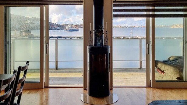 A room with a large sliding glass door leading to a balcony with a view of a harbor and distant buildings. - Beach front home in Rönnäng with sauna (Rönnäng)