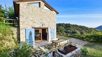 Una casa in pietra con una terrazza in legno, una panchina e un angolo barbecue.