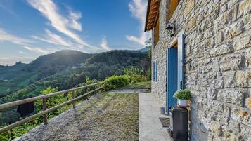 Un edificio in pietra con una porta blu, un piccolo giardino e vista su campi a terrazze e colline.