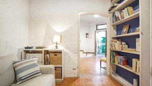 Ein gemütliches Wohnzimmer mit einer Couch, einer Lampe, einem Bücherregal und einem Fliesenboden.