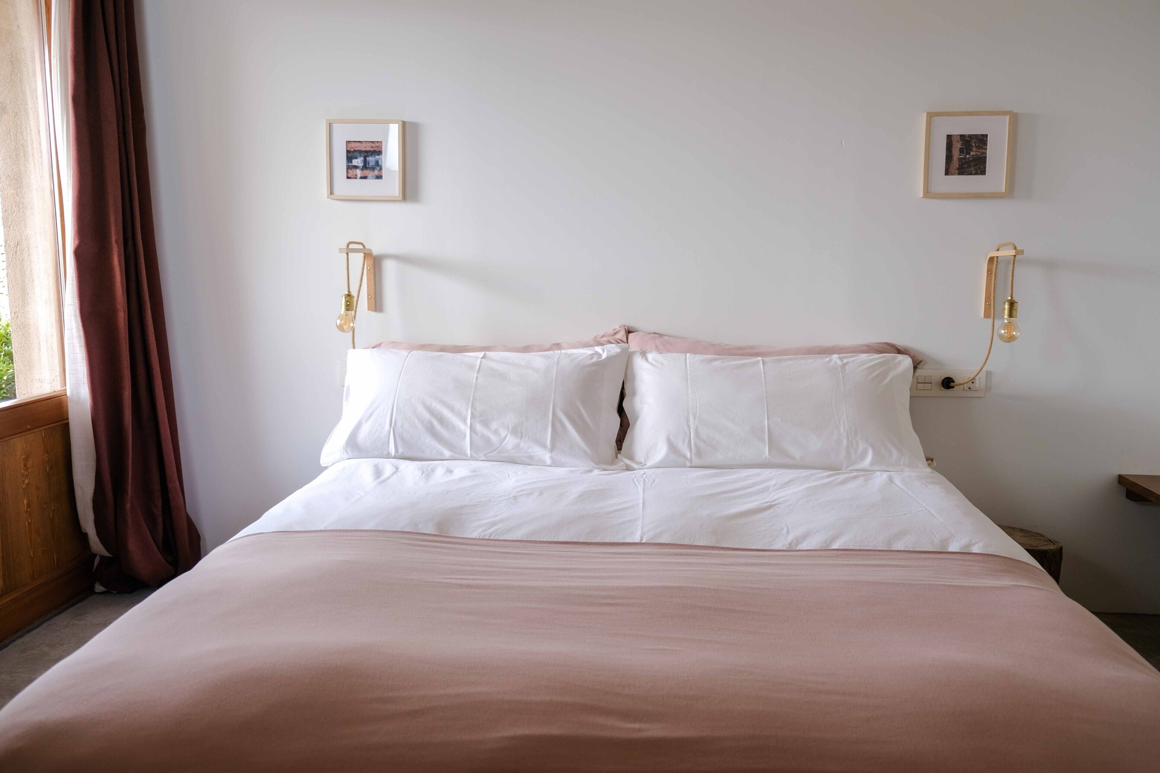 Une chambre à coucher comprenant un lit, deux tables de chevet, une fenêtre avec des rideaux et des luminaires fixés au mur.