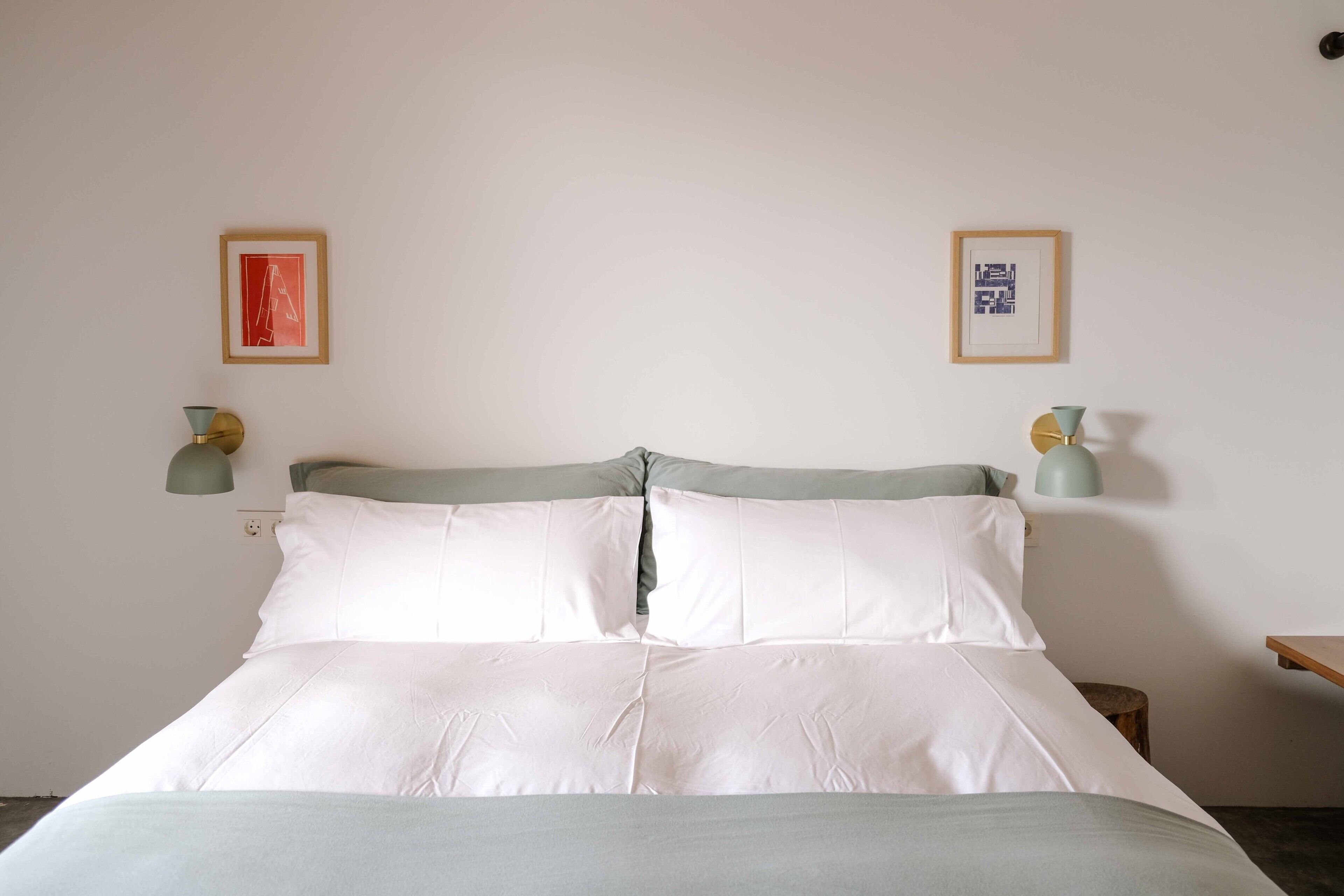 A neatly made bed with white linens, two wall-mounted lamps, and two framed pictures on the wall.