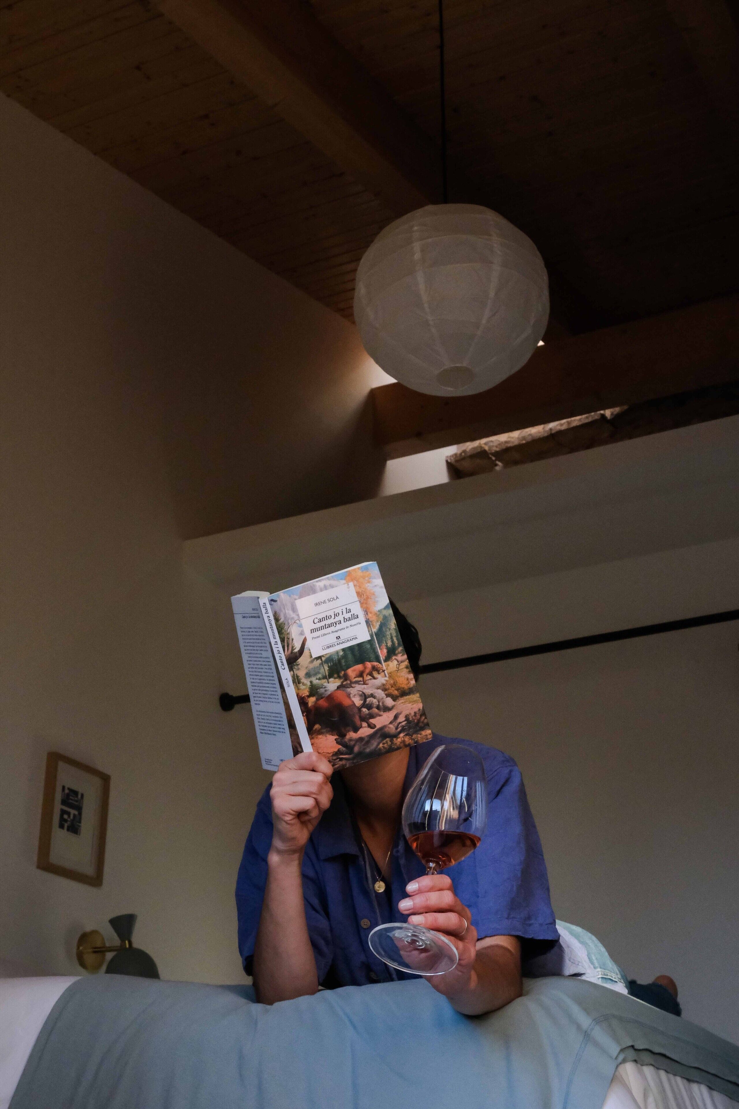 Una persona leyendo una revista y sosteniendo una copa de vino.
