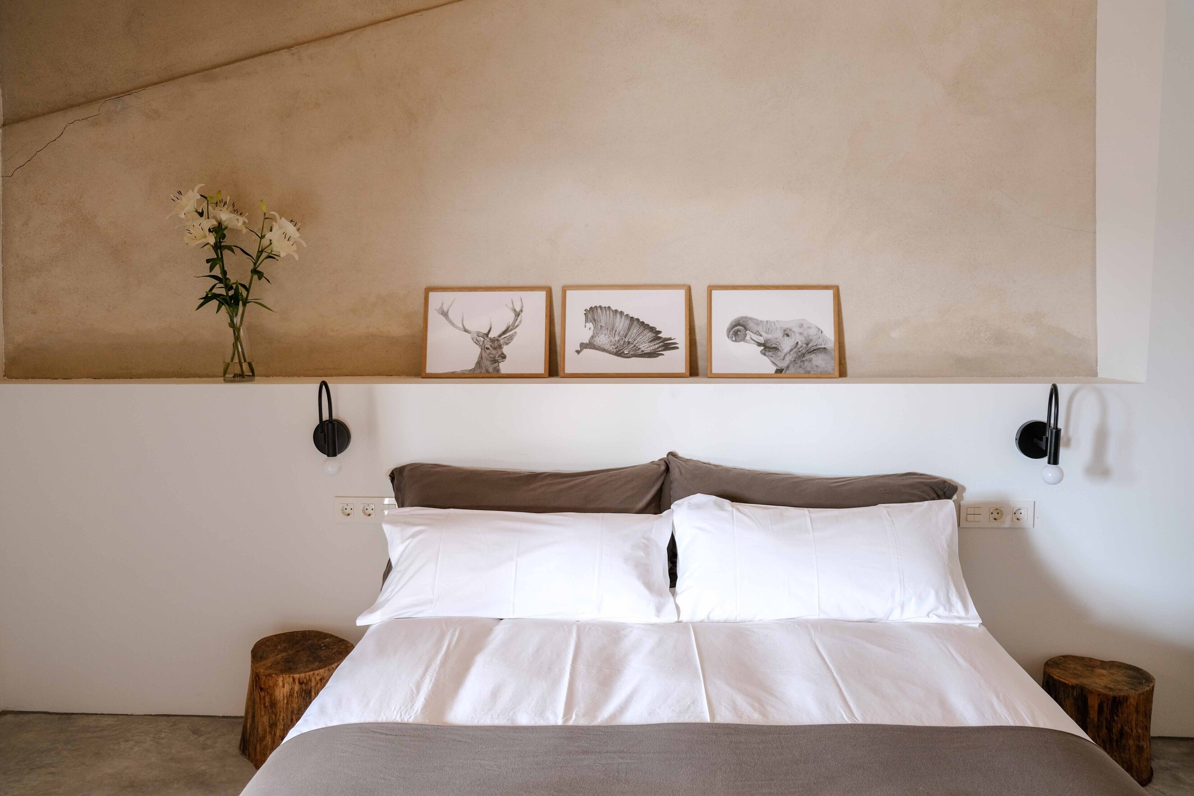 Une chambre à coucher avec un lit, un vase de fleurs et trois illustrations d’animaux encadrées accrochées au mur.