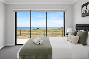 Ein Hotelzimmer mit einem großen Bett, Blick auf den Strand und einem Balkon.