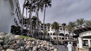 A resort with multiple-story buildings, palm trees, and a pool area with lounge chairs. - Ocean view beach suite (San José del Cabo)