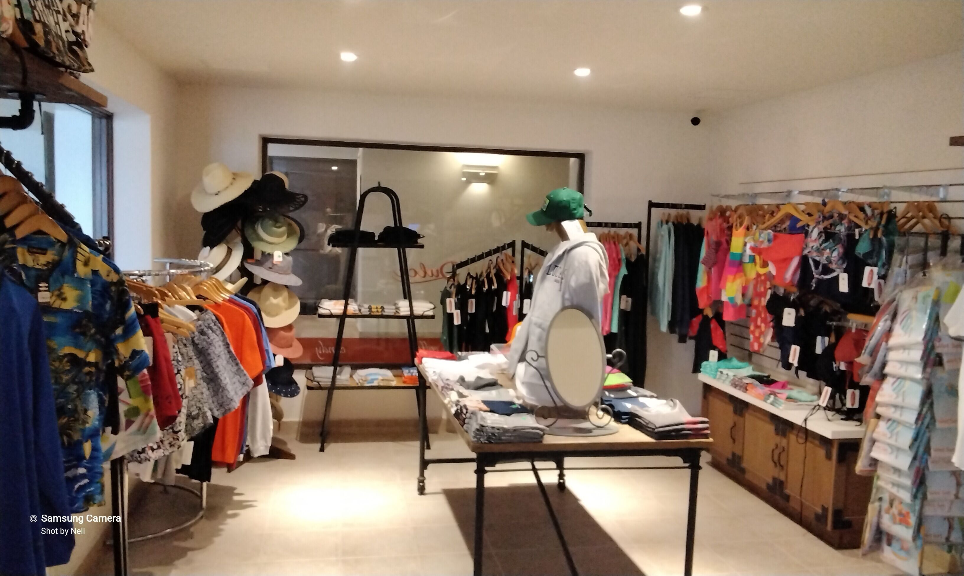 A clothing store with racks of colorful clothes, a mannequin, and a table with folded clothes.