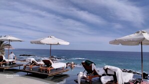 A beachside lounge area with sun loungers, umbrellas, and a poolside setting overlooking the ocean. - Ocean view beach suite (San José del Cabo)