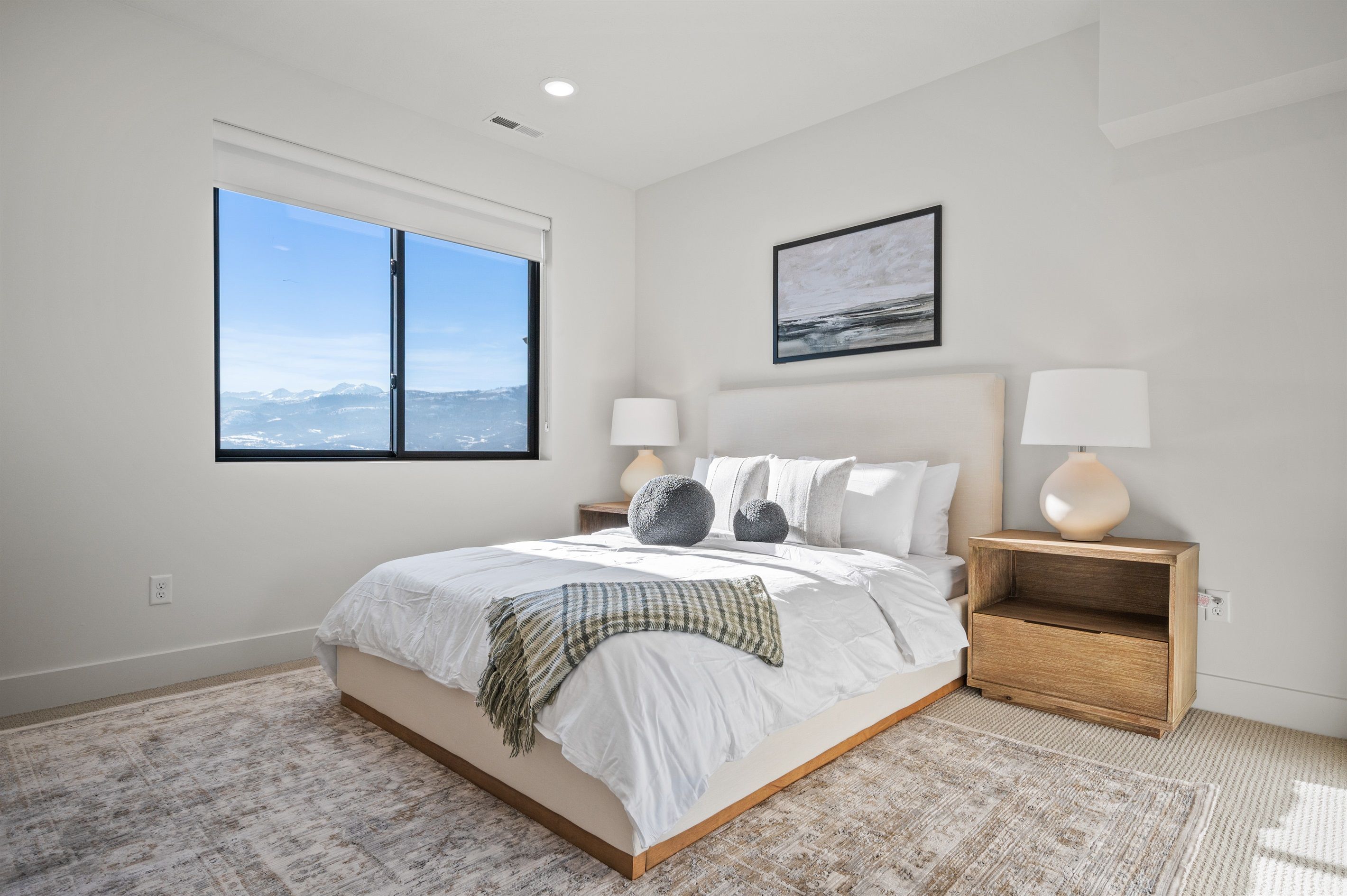 A modern bedroom with a large bed, two bedside tables, a window with a view, and a framed picture on the wall.