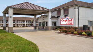 A Crystal Inn hotel with a covered entrance, a parking lot, and a landscaped area with flowers. - Crystal Inn Northeast Houston Downtown I-610 (Houston)