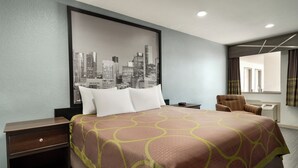A hotel room with a bed, nightstand, chair, and a cityscape artwork on the wall. - Crystal Inn Northeast Houston Downtown I-610 (Houston)