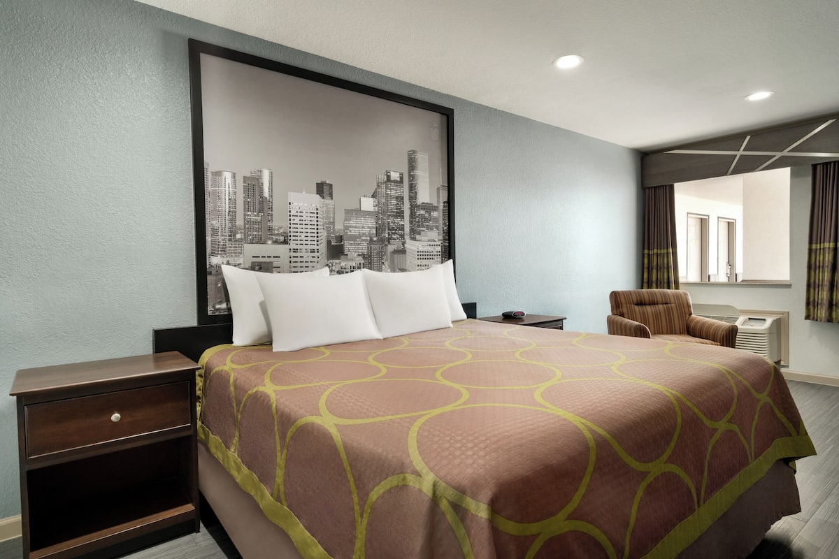 Habitación de hotel con cama, mesita de noche, silla y una obra de arte urbana en la pared.