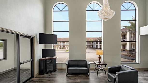 A spacious room with large windows, a flat-screen TV, a sofa, a lamp, and a chandelier. - Crystal Inn Northeast Houston Downtown I-610 (Houston)