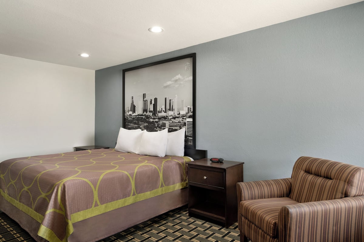Una habitación de hotel con una cama, una silla, una mesita de noche y un cuadro de un paisaje urbano colgado en la pared.