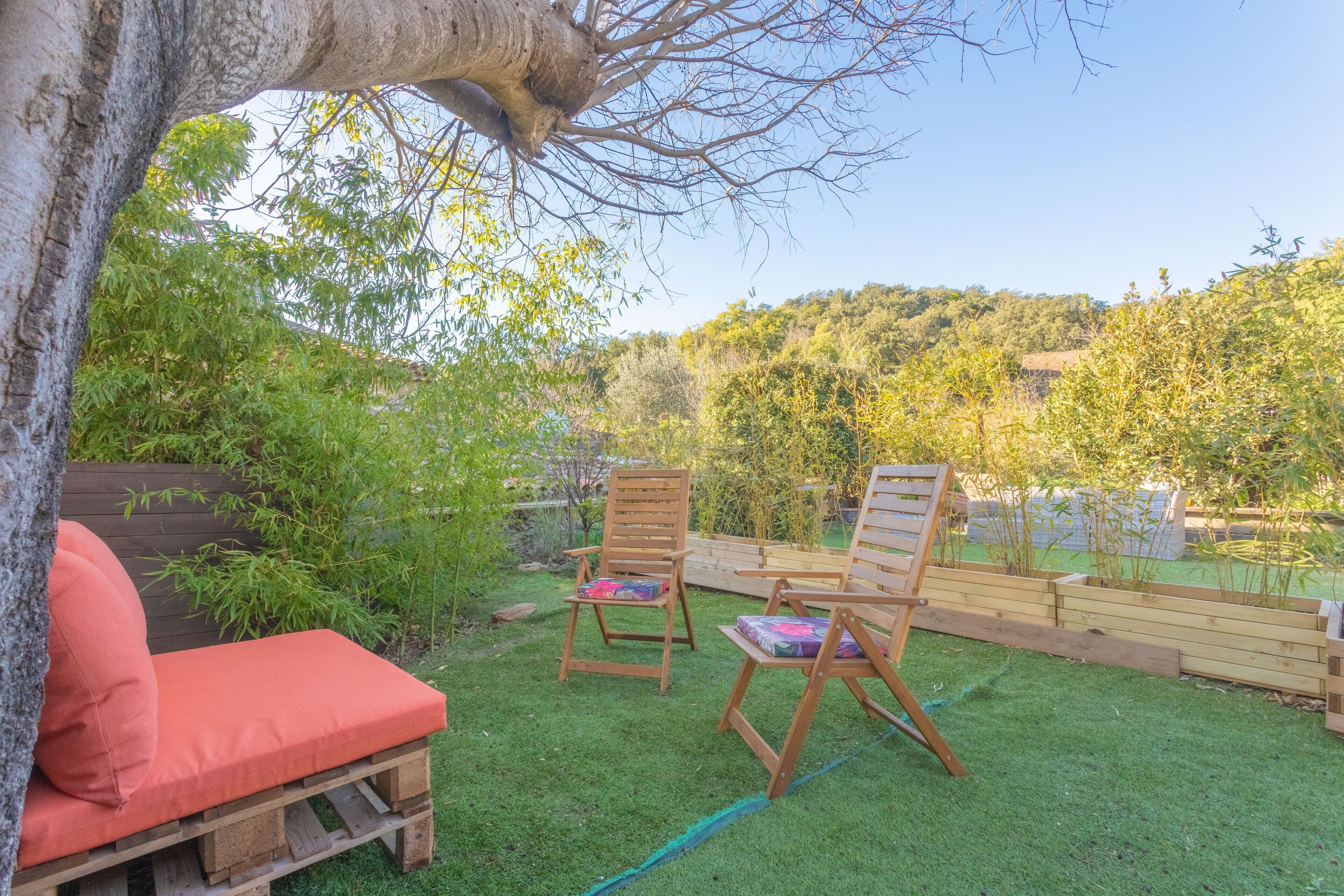 Eine Holzdielen-Terrasse mit zwei Holzstühlen und einer roten gepolsterten Bank.