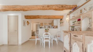 A dining area with a white table and chairs, a wooden ceiling, and a cabinet with decorative items. - Sainte-Maxime House: Private Terrace, Wi-Fi, and Air Conditioning (Le Plan)