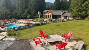 A pool area with red chairs and a fire pit, surrounded by a wooden fence and a building with a porch. - Mara Spring Lodges - Lodge 2 (Mara)