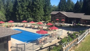 A pool area with red umbrellas, lounge chairs, and a building with outdoor seating. - Mara Spring Lodges - Lodge 2 (Mara)