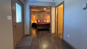 A hallway leading to a bedroom with a bed, bedside lamps, and a painting on the wall. - Mara Spring Lodges - Lodge 2 (Mara)