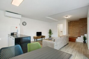 Un salon moderne avec un canapé, une table à manger et un téléviseur. Un escalier mène à un autre niveau.