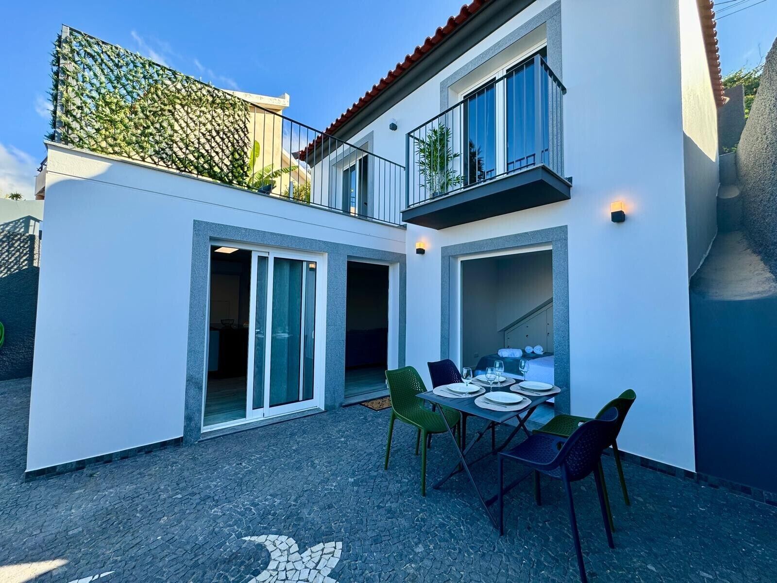 Een modern huis met twee verdiepingen, een terras, een eethoek met stoelen en een tafel, en een balkon met een hekwerk.