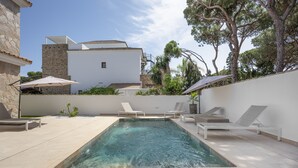 Una piscina con sillas de descanso, un muro de piedra y un edificio con techo de tejas al fondo.