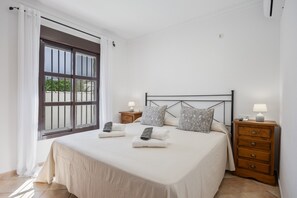 A bedroom with a bed, two bedside tables, a dresser, a window with curtains, and a view outside.