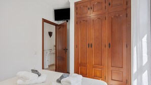 Una habitación de hotel con cama, un armario de madera, televisor montado en la pared y un baño visible a través de una puerta abierta.