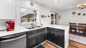 A modern kitchen with black cabinets, a stainless steel dishwasher, and a red coffee maker.