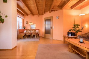 Una habitación acogedora con techo de madera, un comedor con sillas y una mesa, un sofá y una lámpara.