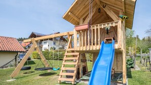 Una casita de juegos de madera con un tobogán, columpios y una escalera.