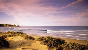 Una playa con dunas de arena y un promontorio rocoso al fondo.