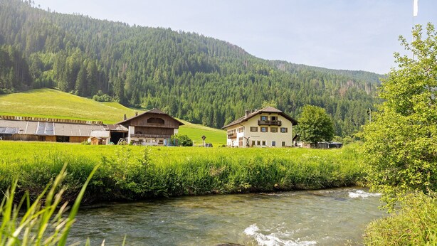 A rural setting with a river, buildings, and a forested hill.
