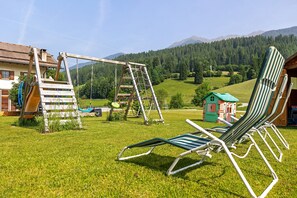 A grassy area with a swing set, a small playhouse, and a row of lawn chairs.