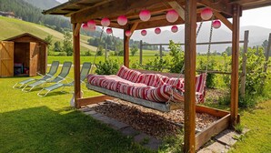 A wooden swing bed with a view of a green field and mountains.