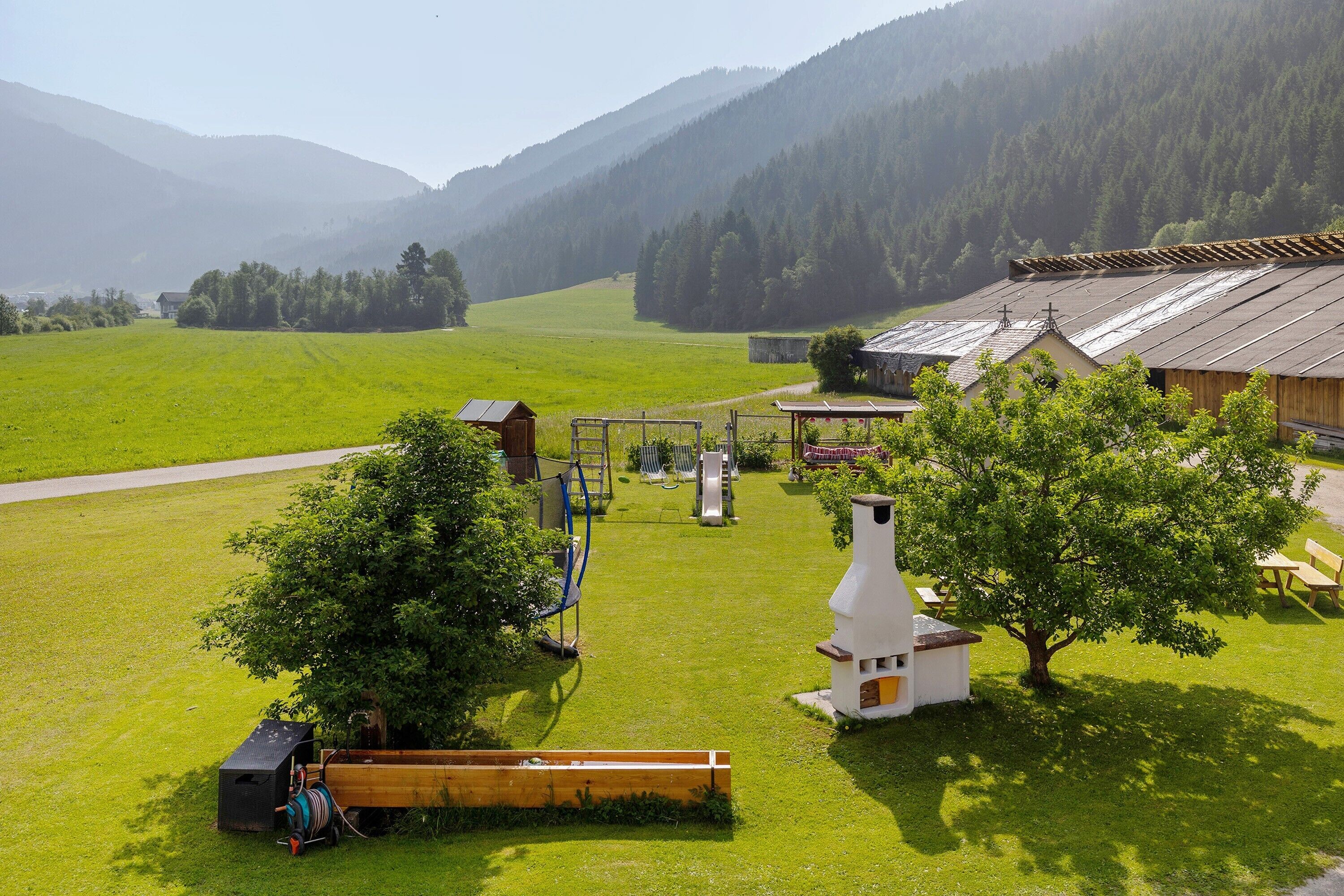 Une propriété rurale dotée d’un grand champ d’herbe, d’une grange en bois, d’une cheminée blanche et d’un petit bâtiment avec un toit en pente.