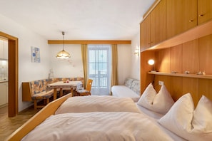 A hotel room with two beds, a dining table, a bench, and a large window with curtains.