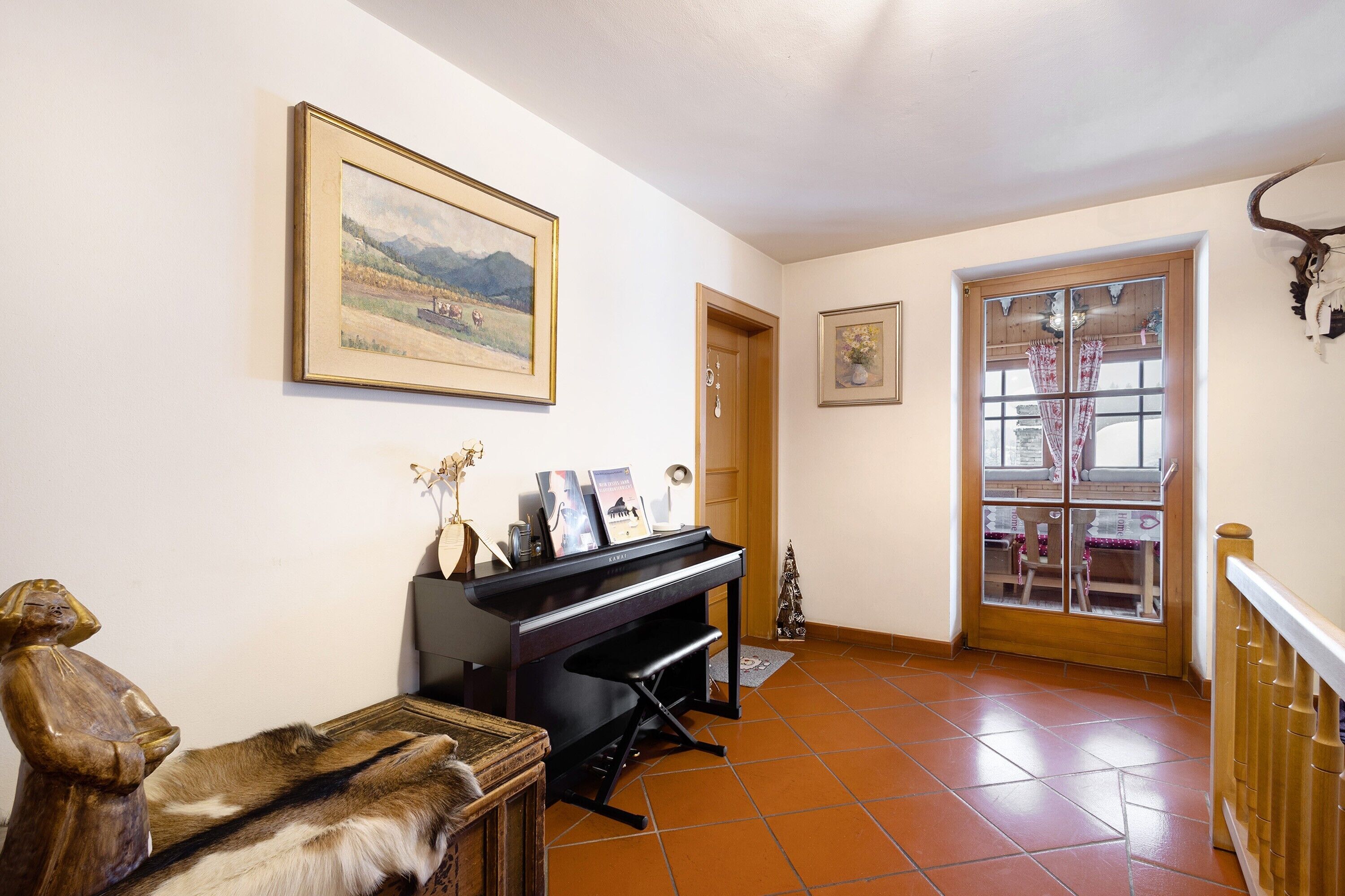 A room with a piano, a wooden statue, a framed landscape painting, and a bull's head mounted on the wall.