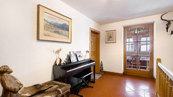 A room with a piano, a wooden statue, a framed landscape painting, and a bull's head mounted on the wall.