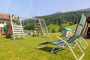 A grassy area with a swing set, a small playhouse, and a row of lawn chairs. - Apartment 'Winter' with Mountain View, Shared Garden and Wi-Fi (Valle di Casies)
