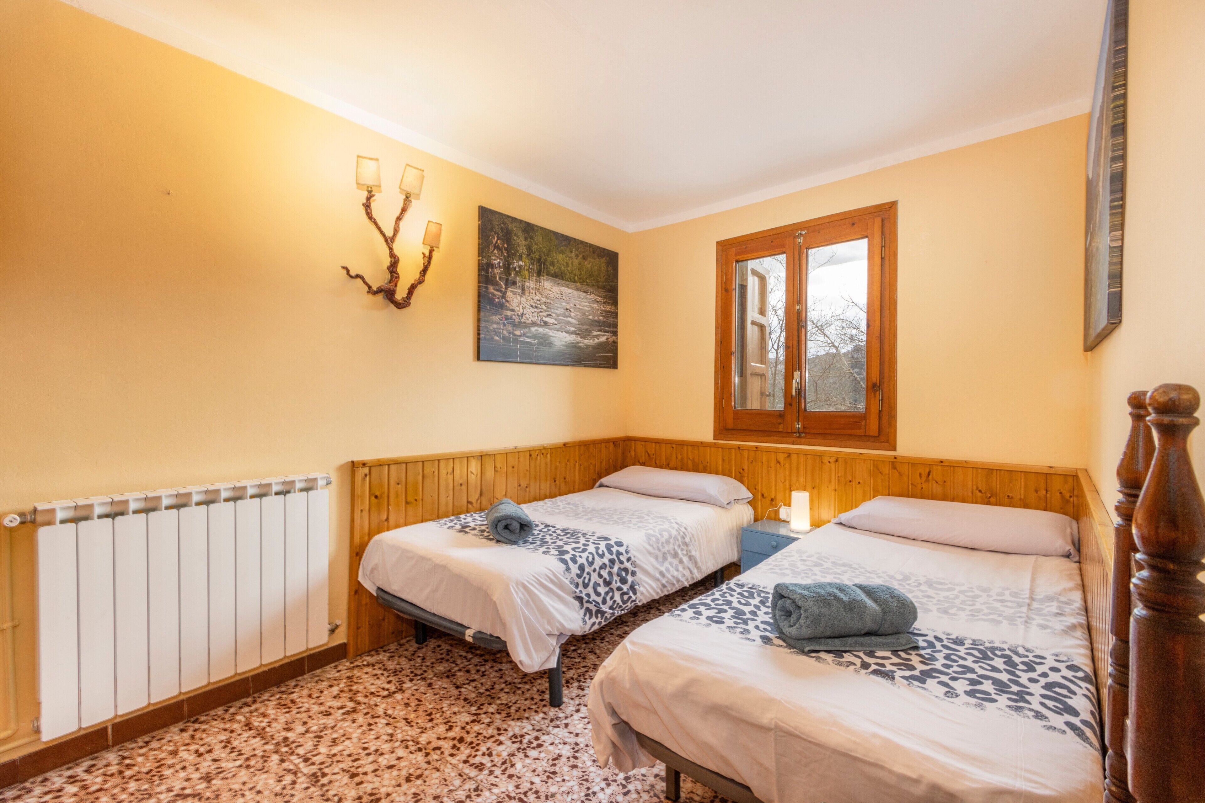 Een slaapkamer met twee bedden, een radiator, een schilderij en een raam.