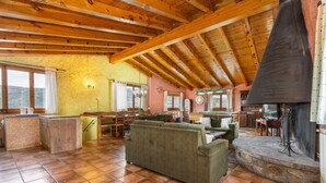 A rustic interior with a wooden ceiling, a stone fireplace, a green sofa, and a kitchen area. - Country House 'Sisquet' with Mountain View, Private Terrace and Wi-Fi (Montcortès)