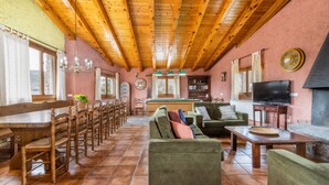 A spacious room with a wooden ceiling, a green sofa, a dining table with chairs, a television, and a fireplace. - Country House 'Sisquet' with Mountain View, Private Terrace and Wi-Fi (Montcortès)