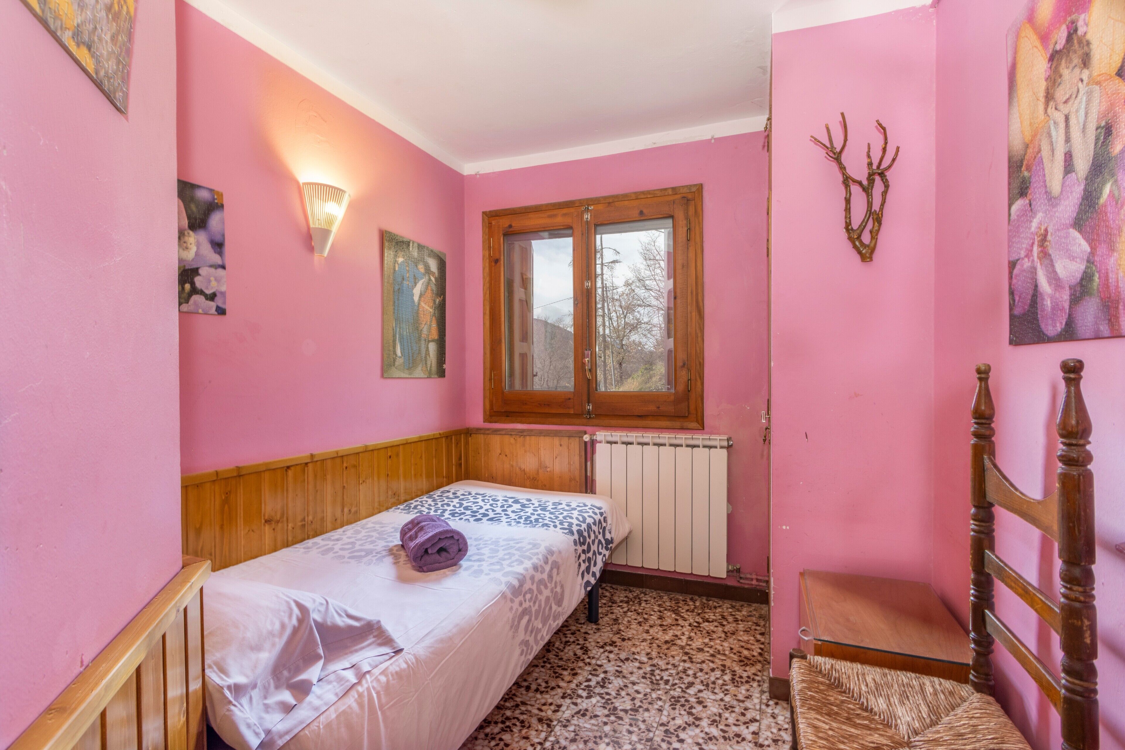 Una habitación rosa con cama, una silla, un radiador y una ventana.