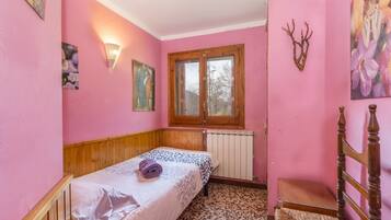 Una habitación rosa con cama, una silla, un radiador y una ventana.