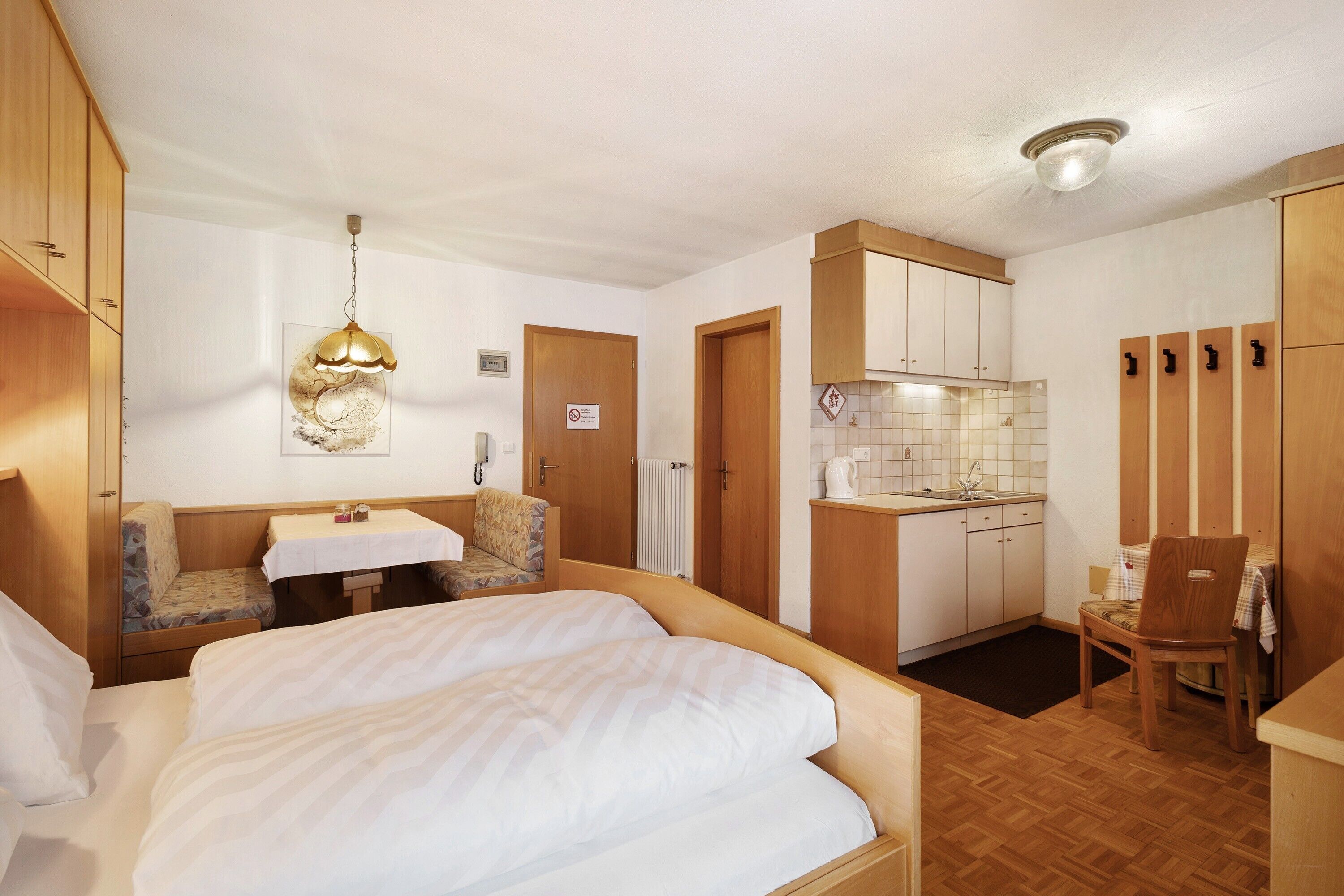 A compact hotel room with a bed, a small table, a kitchenette, and a seating area.