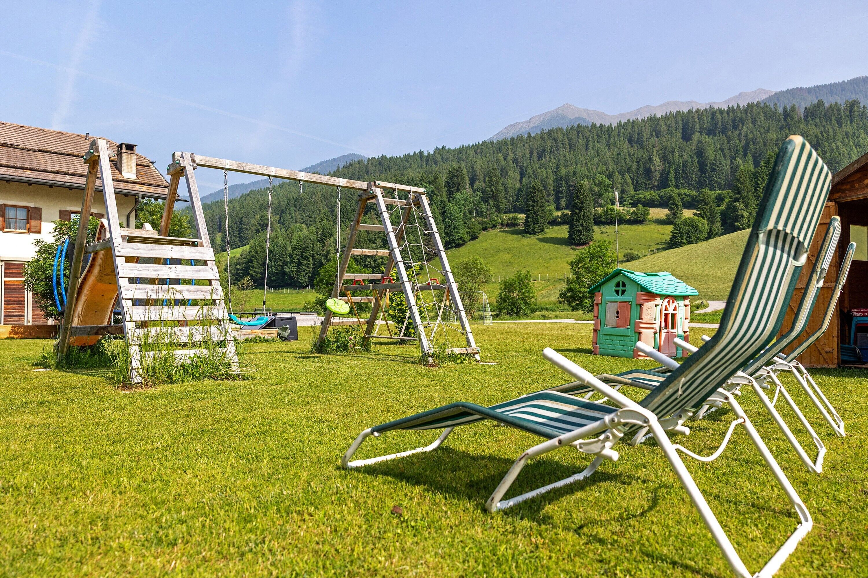 Een gazon met een schommel, een klein speelhuisje en een rij tuinstoelen.