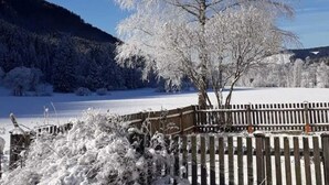 Paisaje nevado con un árbol en primer plano y una estructura de madera a la derecha.