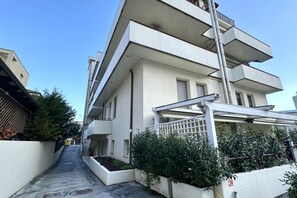 Ein mehrgeschossiges Wohngebäude mit flacher Fassade, einem sichtbaren Balkon im oberen Stockwerk und einem verschlossenen Eingang.