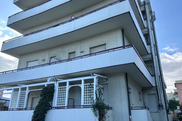 A multi-story building with balconies, a covered outdoor area, and a visible door.